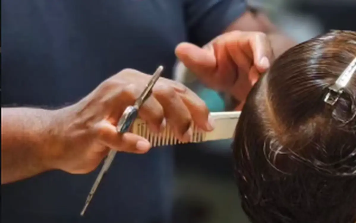 Barbeiro da Espaço Muniz realizando corte masculino com tesoura.
